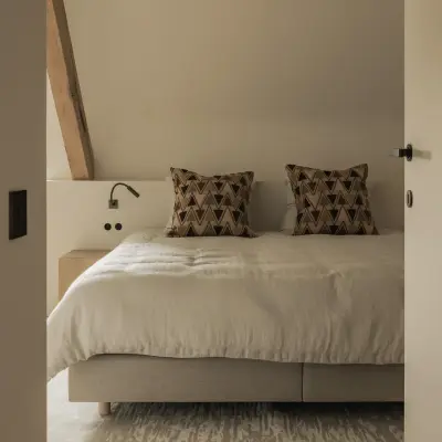 Bed met grafische kussens en leeslampjes op een wollen tapijt, Hoeve in Westkapelle, interieur Laura Calleeuw