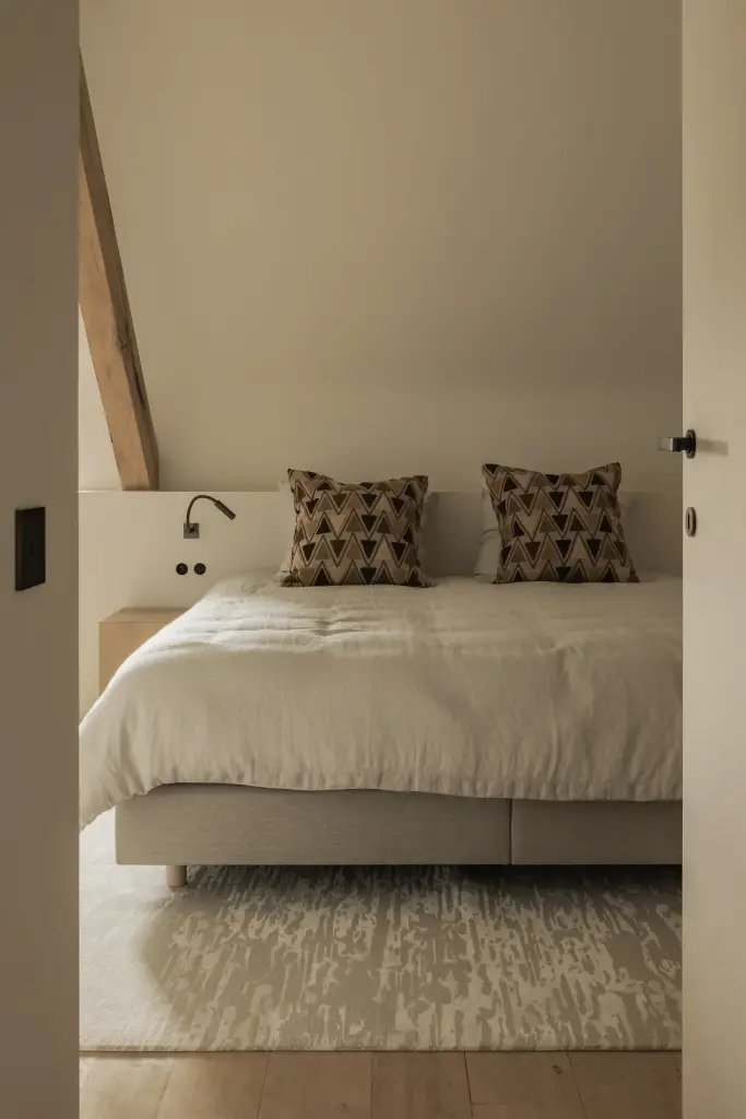 Bed met grafische kussens en leeslampjes op een wollen tapijt, Hoeve in Westkapelle, interieur Laura Calleeuw