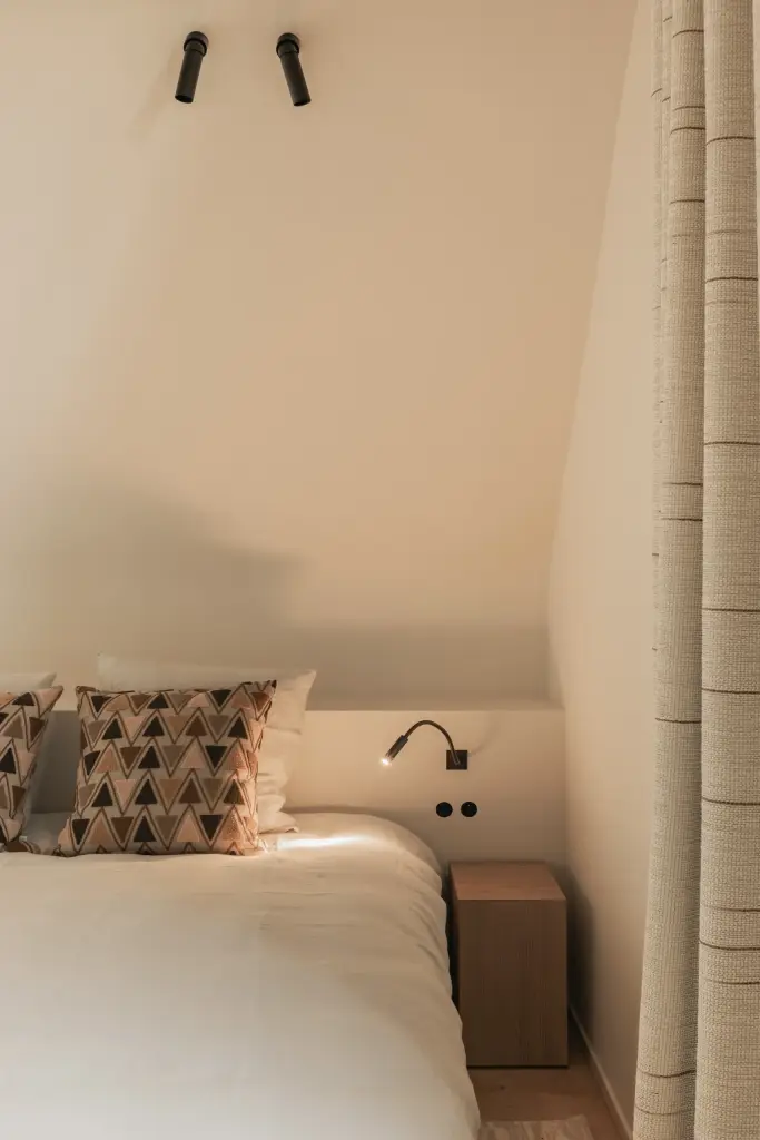 Bed met leeslamp en zwarte spots onder de dakhelling, Hoeve in Westkapelle, interieur Laura Calleeuw