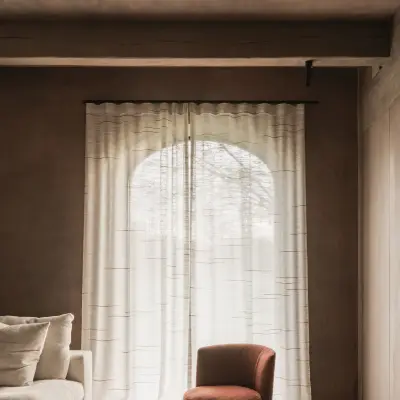 Boogvormig raam met vitrage boven een roestkleurige fauteuil en sofa, Hoeve in Westkapelle, interieur Laura Calleeuw