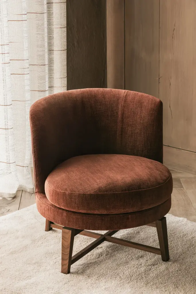 Fauteuil in roestkleurig fluweel met draaivoet in hout op een wit tapijt, Hoeve in Westkapelle, interieur Laura Calleeuw