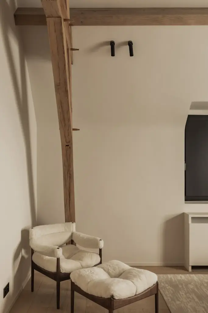 Fauteuil met schapenvacht en poef onder een houten gordingbalk, Hoeve in Westkapelle, interieur Laura Calleeuw