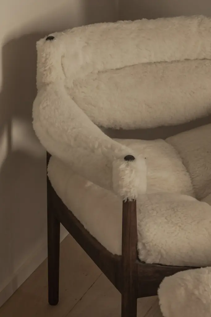 Fauteuil met schapenvacht en poef onder een houten gordingbalk, Hoeve in Westkapelle, interieur Laura Calleeuw