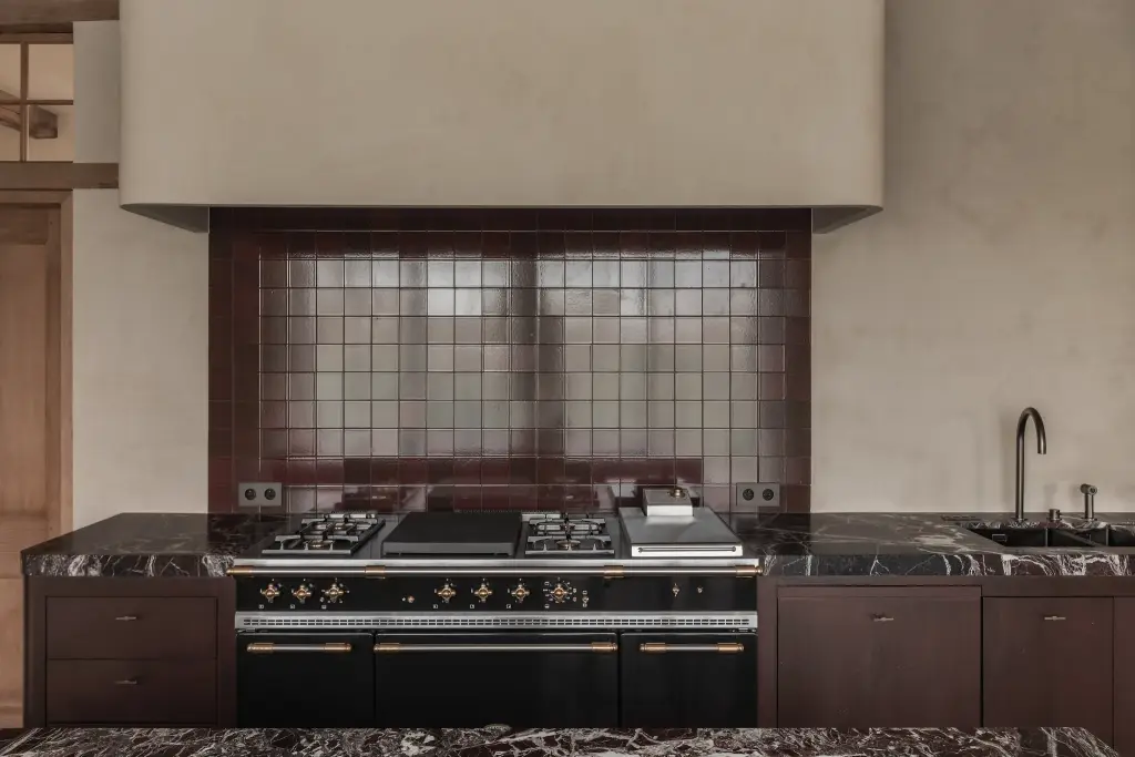 Fornuis met bordeauxkleurig tegelwerk onder een gepleisterde schouw in de keuken, Hoeve in Westkapelle, interieur Laura Calleeuw