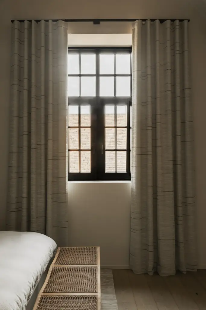 Gordijn voor een zwart raam met een rotan bank aan het bed, Hoeve in Westkapelle, interieur Laura Calleeuw