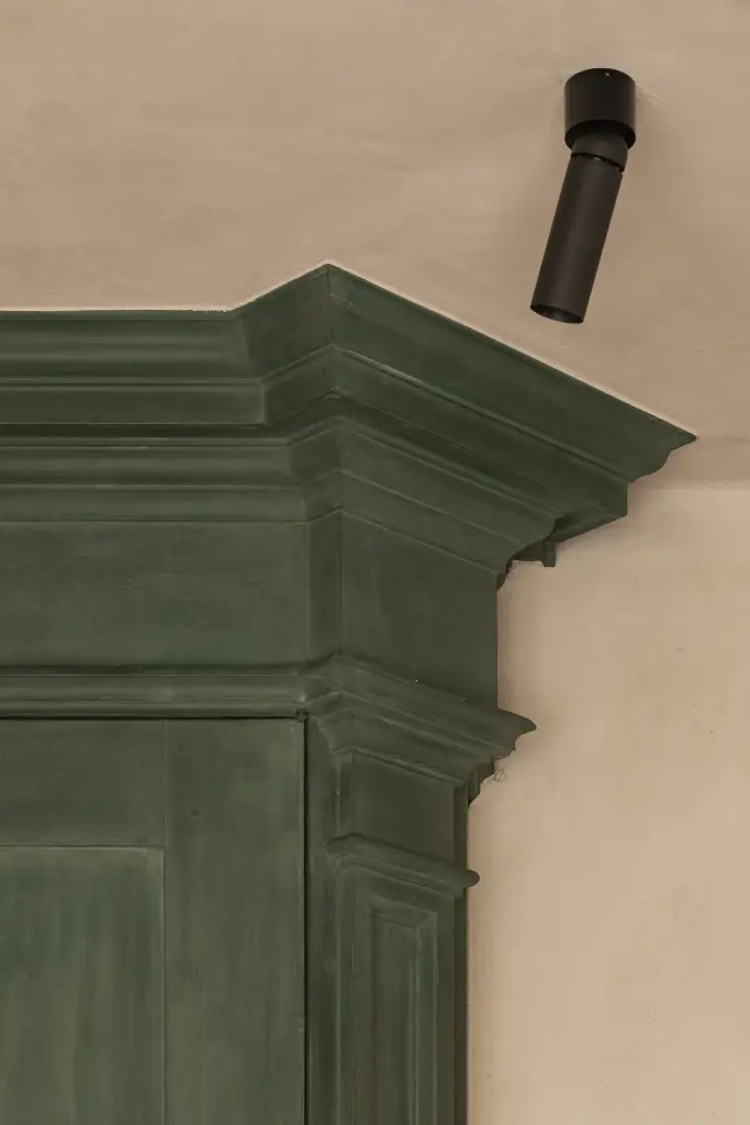 Detail van het lijstwerk op de groen geschilderde kast naast een zwarte spot, Hoeve in Westkapelle, interieur Laura Calleeuw