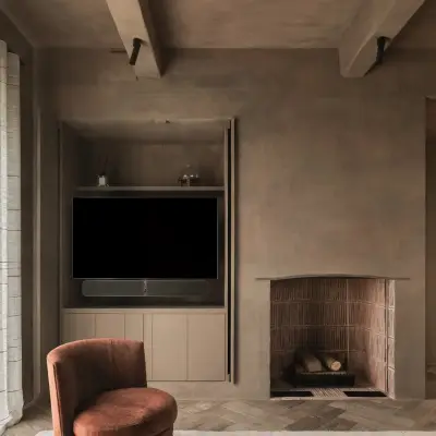 Zitkamer met haardnis, houten kasten, televisie in de kast en een roestkleurige fauteuil op het visgraatparket, Hoeve in Westkapelle, interieur Laura Calleeuw