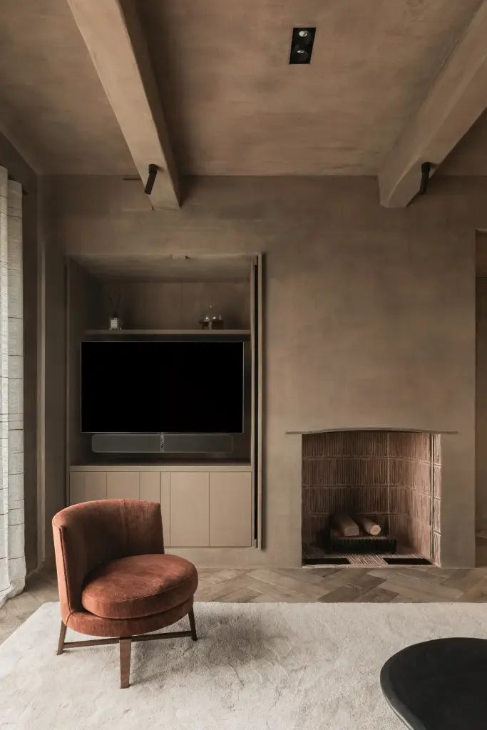 Zitkamer met haardnis, houten kasten, televisie in de kast en een roestkleurige fauteuil op het visgraatparket, Hoeve in Westkapelle, interieur Laura Calleeuw