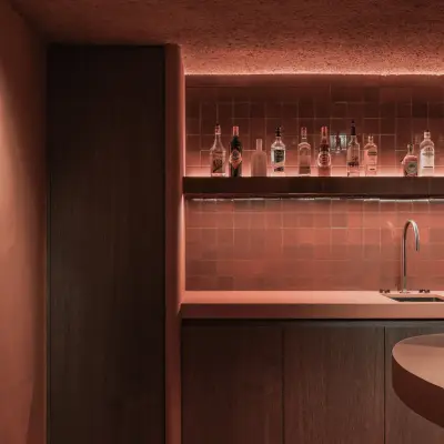 Verlichte flessenwand met kast in donker hout in de kelderbar, Hoeve in Westkapelle, interieur Laura Calleeuw
