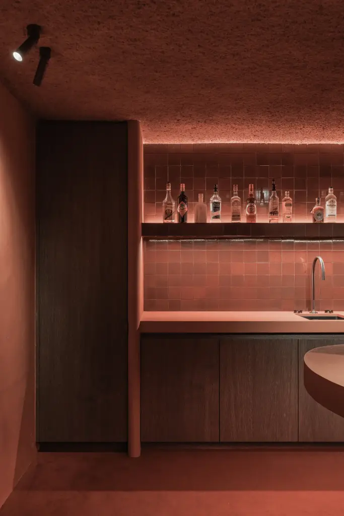 Verlichte flessenwand met kast in donker hout in de kelderbar, Hoeve in Westkapelle, interieur Laura Calleeuw