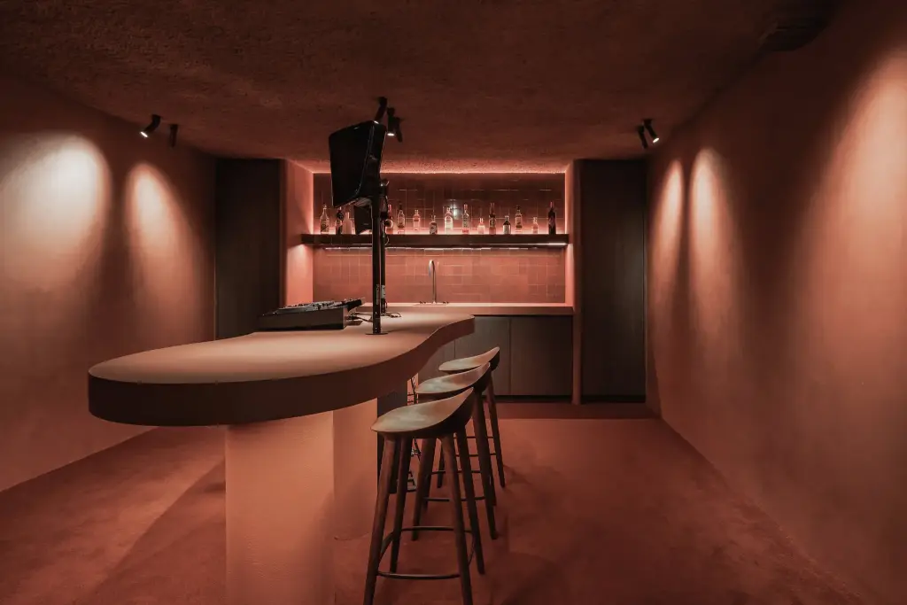 Kelderbar in terracotta met ronde toog, barkrukken en verlichte flessenwand, Hoeve in Westkapelle, interieur Laura Calleeuw