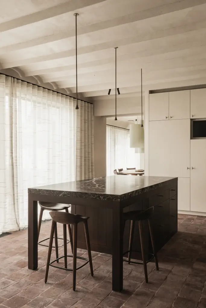 Keuken met kookeiland, barkrukken en lange gordijnen voor het raam onder gekalkte balken, Hoeve in Westkapelle, interieur Laura Calleeuw