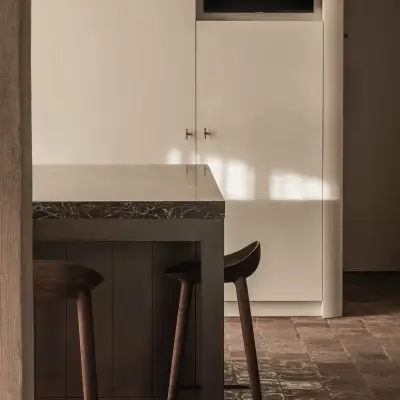 Witte keukenkasten met televisie en het kookeiland met barkrukken, Hoeve in Westkapelle, interieur Laura Calleeuw