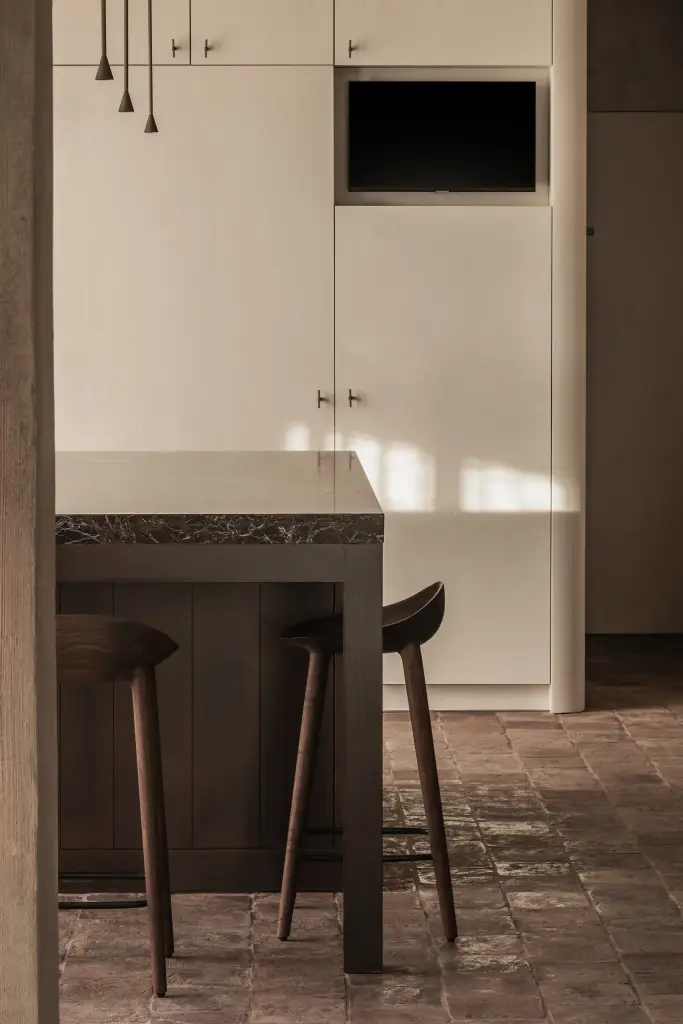Witte keukenkasten met televisie en het kookeiland met barkrukken, Hoeve in Westkapelle, interieur Laura Calleeuw