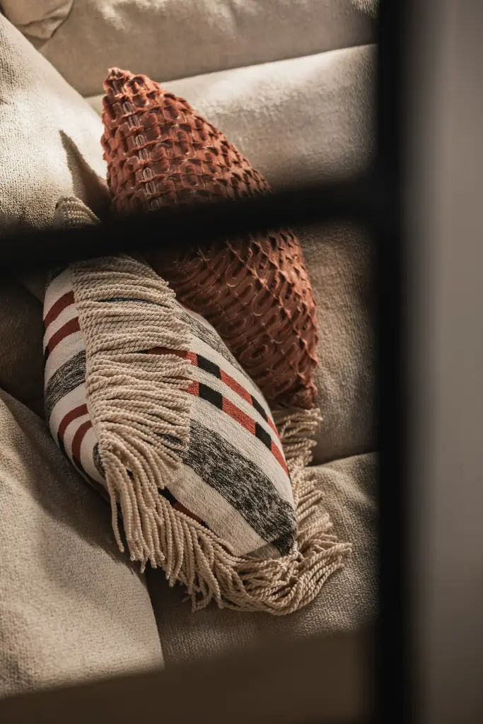 Detail van kussens met franjes en een patroon naast een zwart raamkader, Hoeve in Westkapelle, interieur Laura Calleeuw