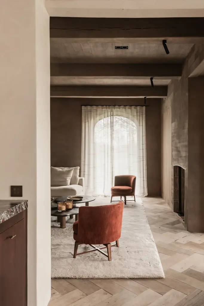 Leefruimte met boogvormig raam, roestkleurige fauteuil en visgraatparket, Hoeve in Westkapelle, interieur Laura Calleeuw