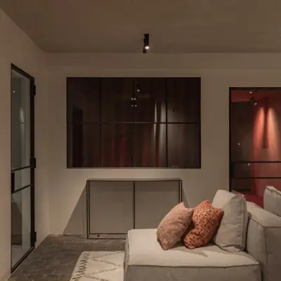 Lounge in de kelder met zetel, rode deuren en een stalen glaswand, Hoeve in Westkapelle, interieur Laura Calleeuw