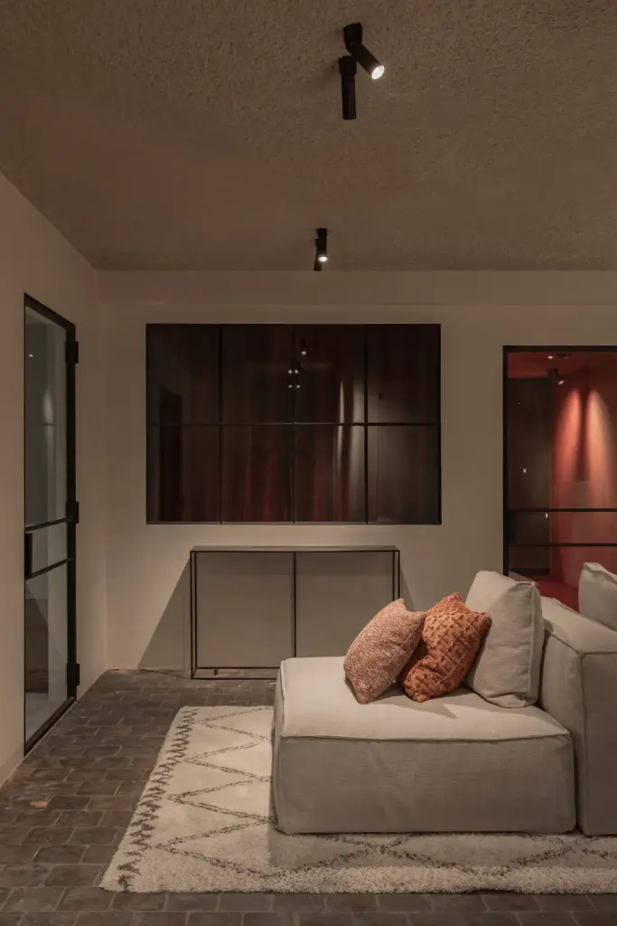 Lounge in de kelder met zetel, rode deuren en een stalen glaswand, Hoeve in Westkapelle, interieur Laura Calleeuw