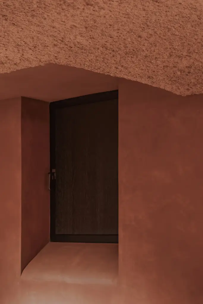 Nis met donkere deur in de terracotta wand onder een gestructureerd plafond, Hoeve in Westkapelle, interieur Laura Calleeuw