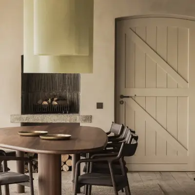Open haard met houtstapel, eettafel en een wit gelatteerde deur, Hoeve in Westkapelle, interieur Laura Calleeuw