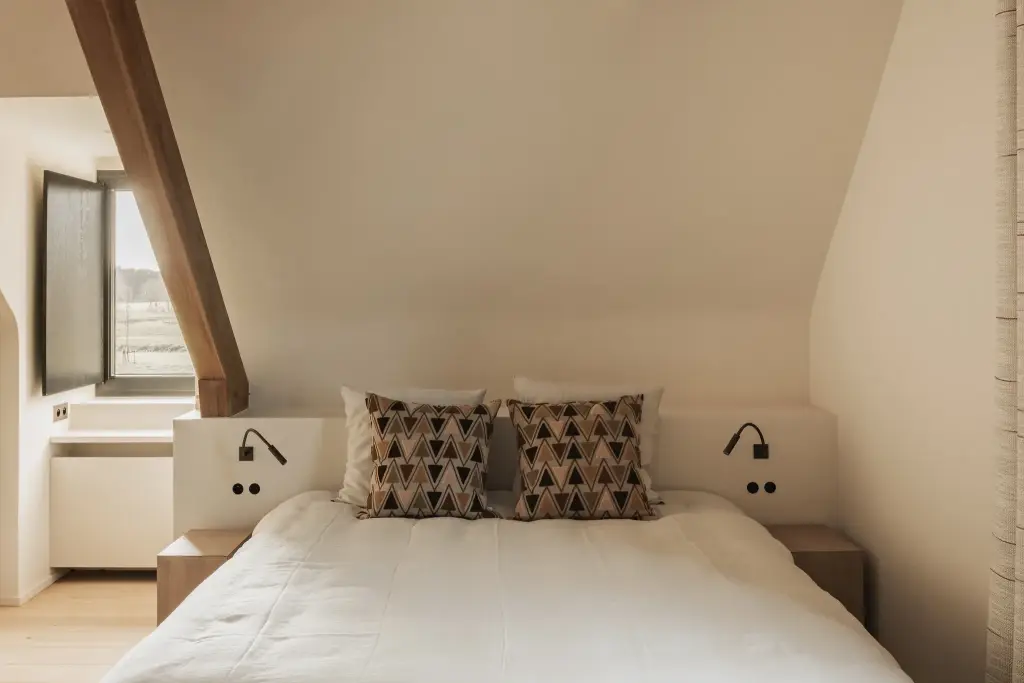 Slaapkamer onder de dakhelling met bed, leeslampjes en doorkijk naar de badkamer, Hoeve in Westkapelle, interieur Laura Calleeuw