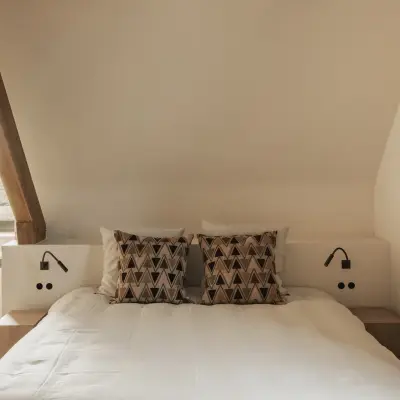 Slaapkamer onder de dakhelling met bed, leeslampjes en doorkijk naar de badkamer, Hoeve in Westkapelle, interieur Laura Calleeuw