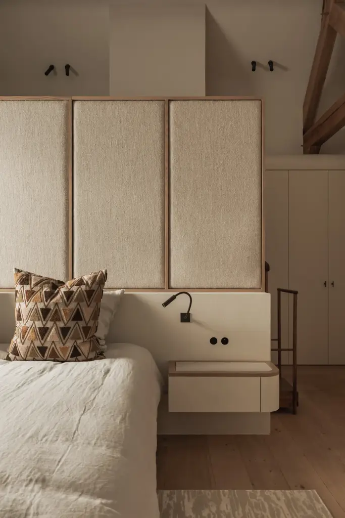 Slaapkamer met hoog gestoffeerd hoofdbord in linnen, leeslampjes en kussens met grafisch patroon, Hoeve in Westkapelle, interieur Laura Calleeuw
