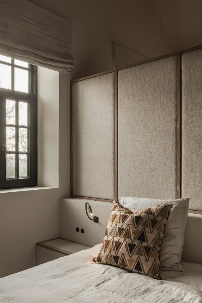 Slaapkamer met hoofdbord, kussen en een zwart raam met roman blind, Hoeve in Westkapelle, interieur Laura Calleeuw