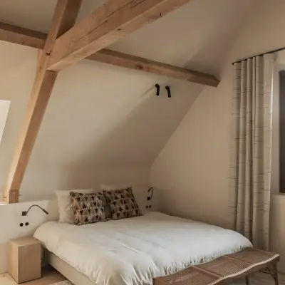 Slaapkamer onder houten balken met bed, houten bank en een wollen tapijt, Hoeve in Westkapelle, interieur Laura Calleeuw
