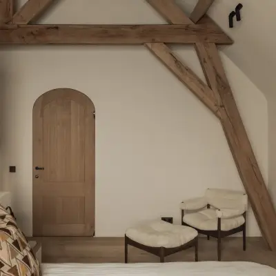 Slaapkamer onder houten balken met een eikenhouten boogdeur en twee fauteuils met schapenvacht, Hoeve in Westkapelle, interieur Laura Calleeuw