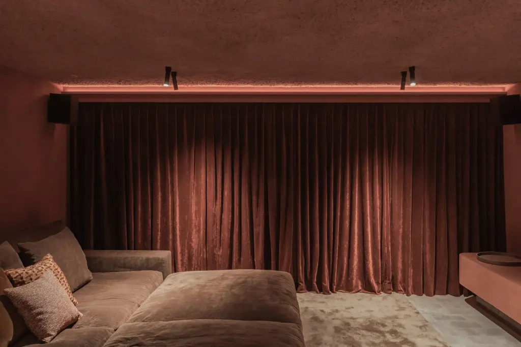 Thuisbioscoop met fluwelen gordijn, grote sofa en een lichtlijn boven het scherm, Hoeve in Westkapelle, interieur Laura Calleeuw