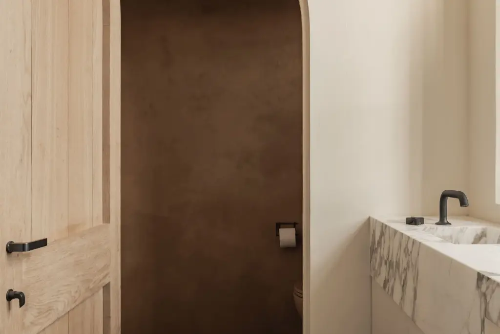 Marmeren wastafel met zwarte kraan en een eikenhouten deur naar het toilet in leempleister, Hoeve in Westkapelle, interieur Laura Calleeuw