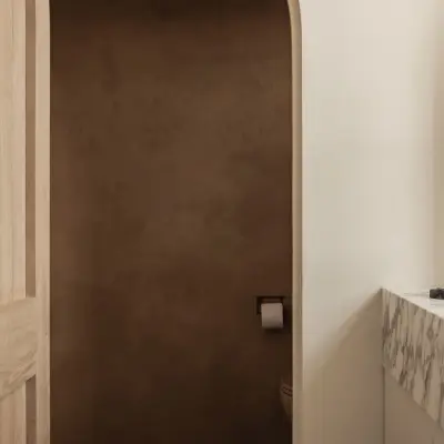 Marmeren wastafel met zwarte kraan en een eikenhouten deur naar het toilet in leempleister, Hoeve in Westkapelle, interieur Laura Calleeuw