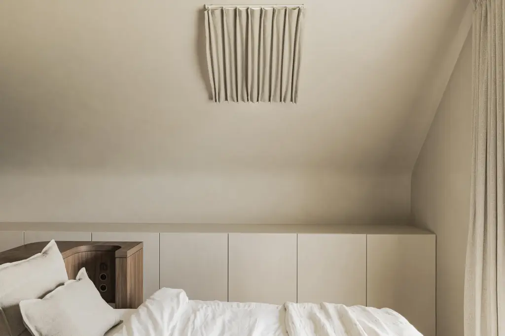 Bed met kussens naast kasten onder de dakhelling en een gordijnrail, a masterful balance between authenticity and comfort, interieur Laura Calleeuw