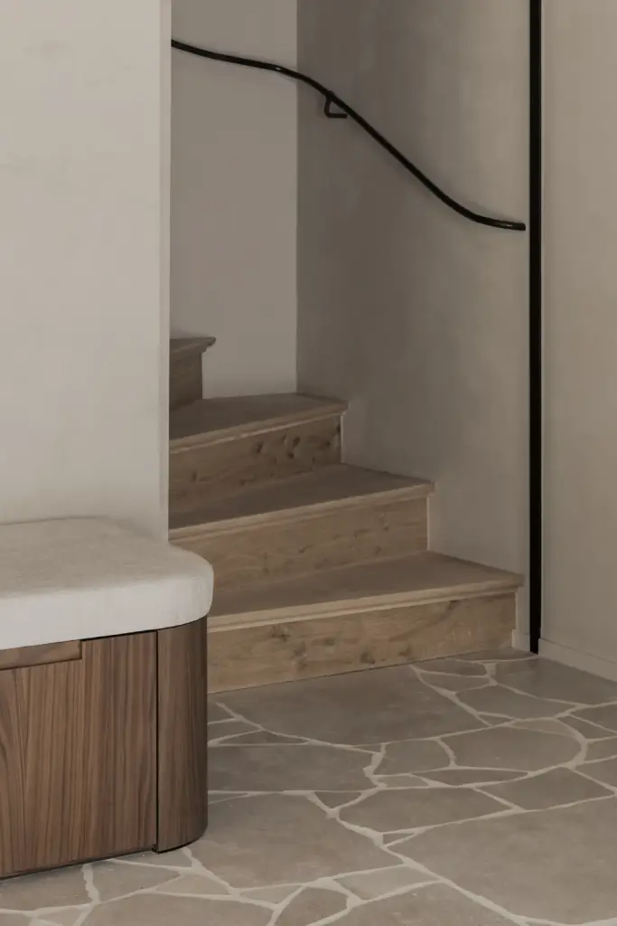 Trap met houten treden, zwarte leuning en gebogen zitbank op een natuurstenen vloer, a masterful balance between authenticity and comfort, interieur Laura Calleeuw