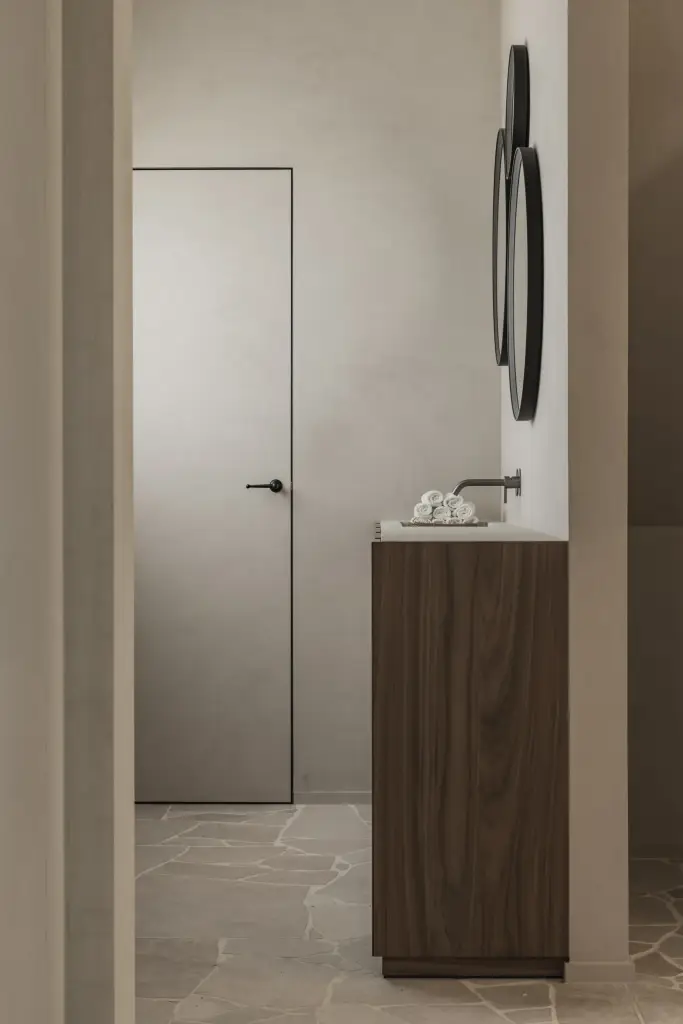 Wastafelmeubel met ronde spiegel naast een vlakke deur op een natuurstenen vloer, a masterful balance between authenticity and comfort, interieur Laura Calleeuw