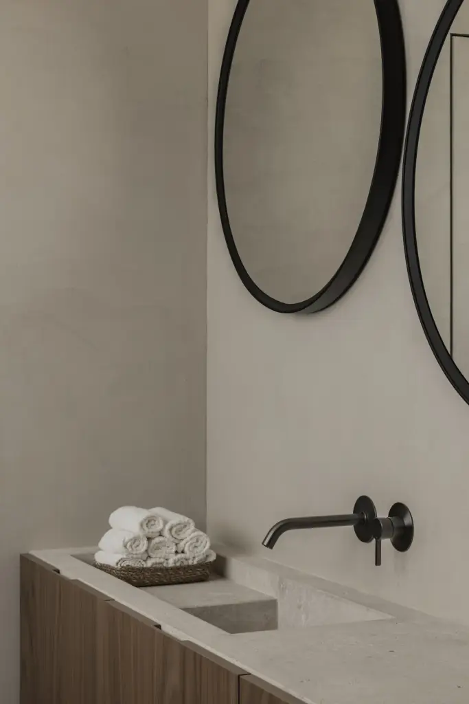 Wastafel in natuursteen met zwarte wandkraan, ronde spiegels en opgerolde handdoeken, a masterful balance between authenticity and comfort, interieur Laura Calleeuw