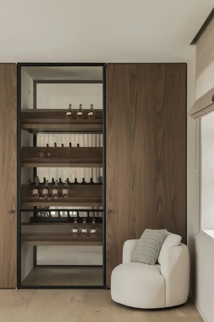 Wijnkast in staal en glas met notelaren zijwand en een fauteuil, a masterful balance between authenticity and comfort, interieur Laura Calleeuw