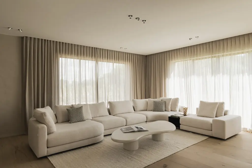 Leefruimte met hoeksofa, organische salontafel en lange gordijnen voor grote ramen, a masterful balance between authenticity and comfort, interieur Laura Calleeuw