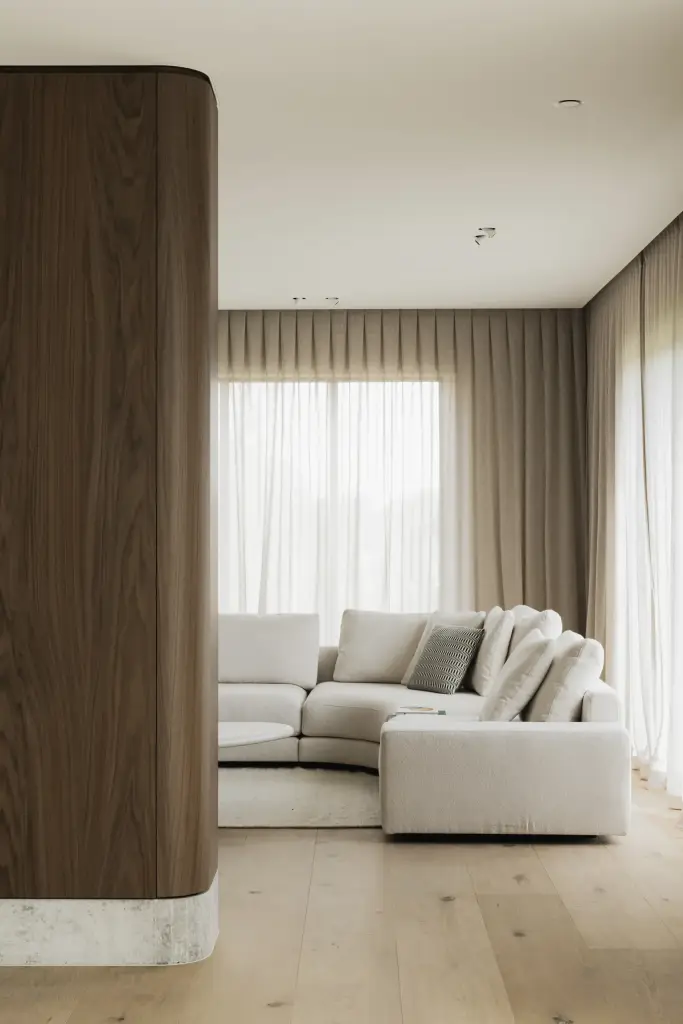Zithoek met hoeksofa achter een gebogen kastvolume in notelaar met natuurstenen plint, a masterful balance between authenticity and comfort, interieur Laura Calleeuw