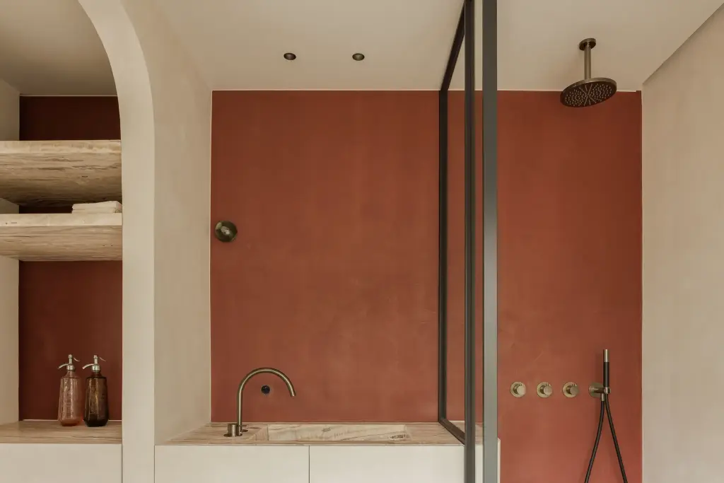 Badkamer met terracotta pleisterwand, regendouche, wastafel en verlichte nis met planken in natuursteen, Villarenovatie in Knokke, interieur Laura Calleeuw