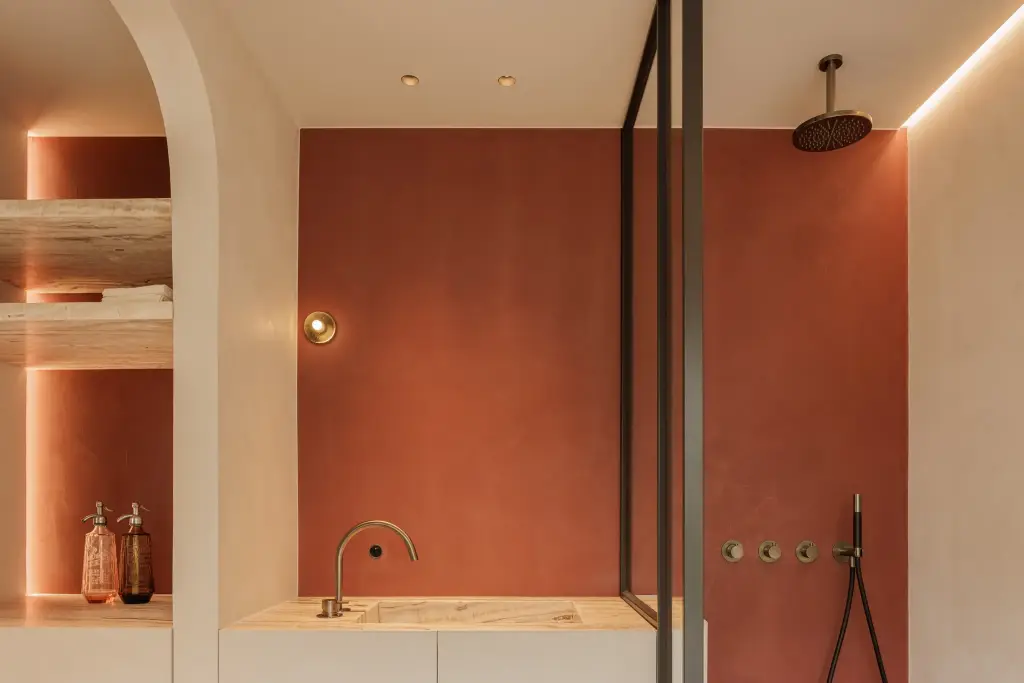 Badkamer met terracotta pleisterwand, regendouche, wastafel en verlichte nis met planken in natuursteen, Villarenovatie in Knokke, interieur Laura Calleeuw