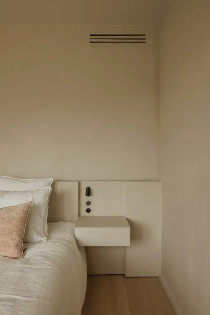 Bed met zwevend nachtkastje, kussens en een zwarte wandlamp, Villarenovatie in Knokke, interieur Laura Calleeuw