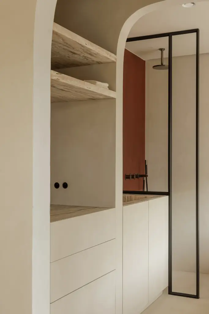 Boogvormige doorgang met natuurstenen planken en een stalen glaswand naar de douche, Villarenovatie in Knokke, interieur Laura Calleeuw