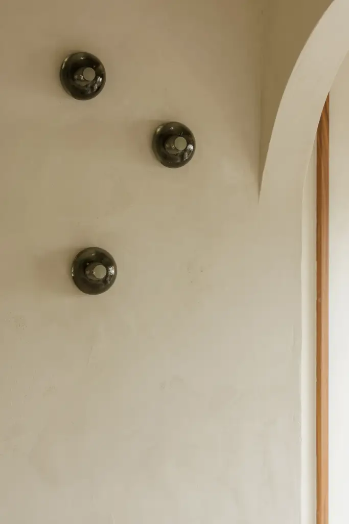 Drie bronzen wandlampjes tegen een kalkpleisterwand naast een boogvormige nis, Villarenovatie in Knokke, interieur Laura Calleeuw