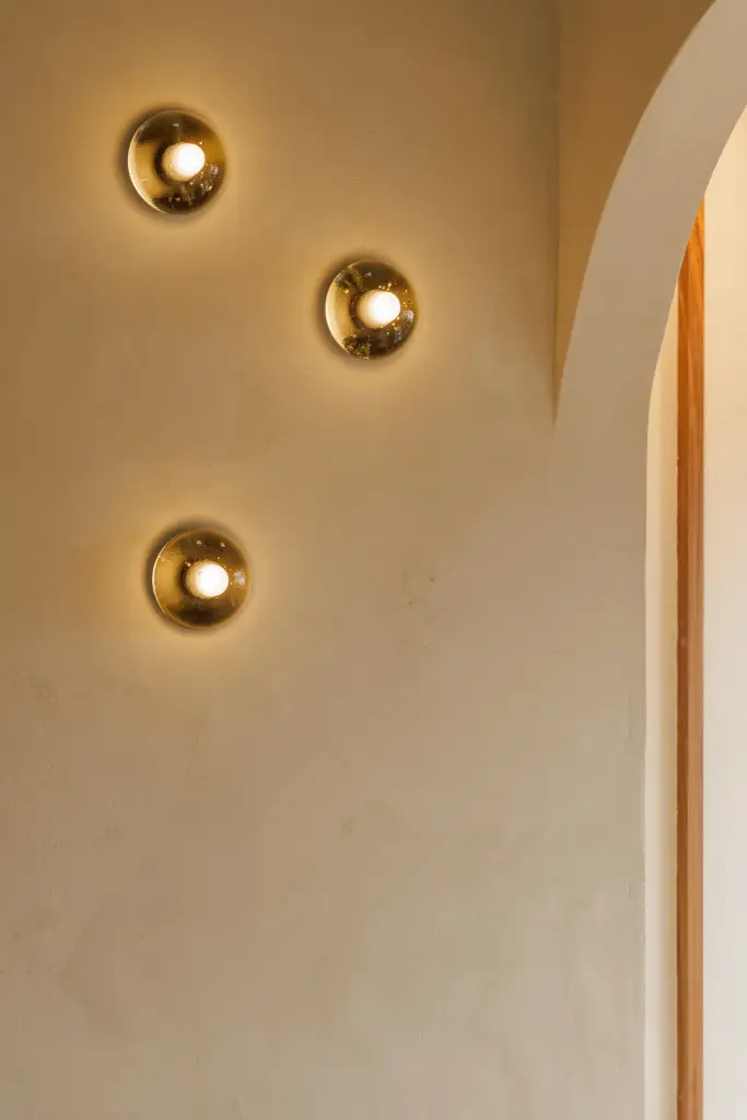 Drie bronzen wandlampjes tegen een kalkpleisterwand naast een boogvormige nis, Villarenovatie in Knokke, interieur Laura Calleeuw