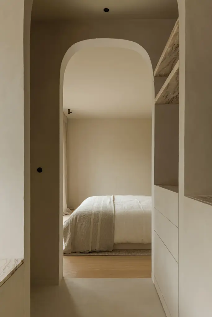 Boogvormige doorgang tussen slaapkamer en badkamer met open planken in natuursteen, Villarenovatie in Knokke, interieur Laura Calleeuw