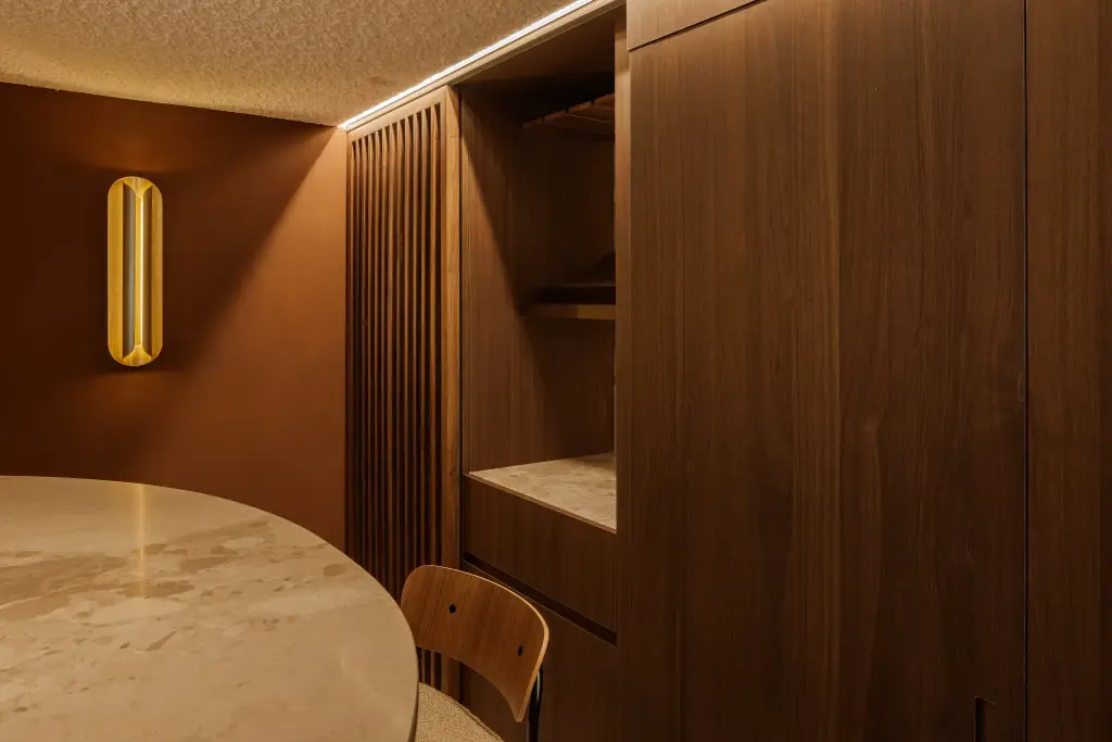 Eetnis met notelaren lamellenwand, ronde natuurstenen tafel, stoel en gouden wandlamp, Villarenovatie in Knokke, interieur Laura Calleeuw