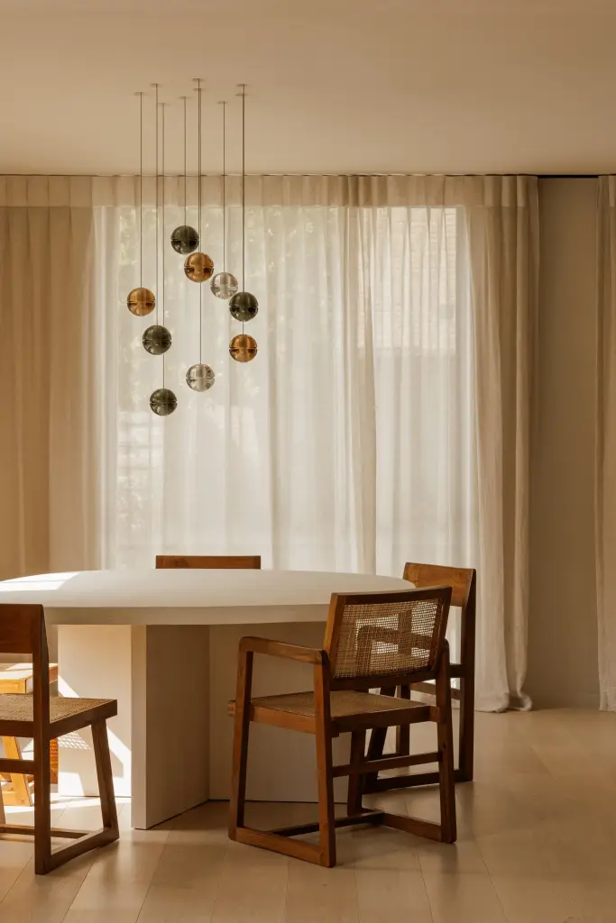 Eettafel met houten stoelen, glazen hanglampen en lange vitrage, Villarenovatie in Knokke, interieur Laura Calleeuw