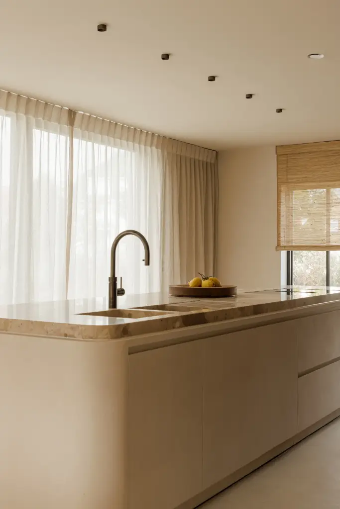 Keuken met kookeiland, spoelbak en zwarte kraan voor een raam met vitrage, Villarenovatie in Knokke, interieur Laura Calleeuw